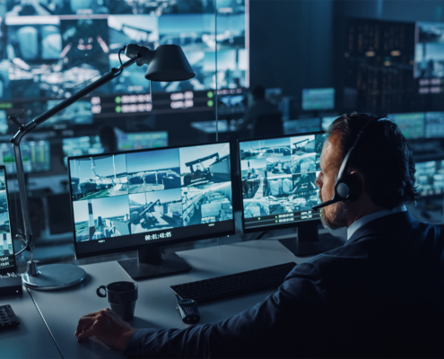 Male Officer Works on a Computer with Surveillance CCTV Video